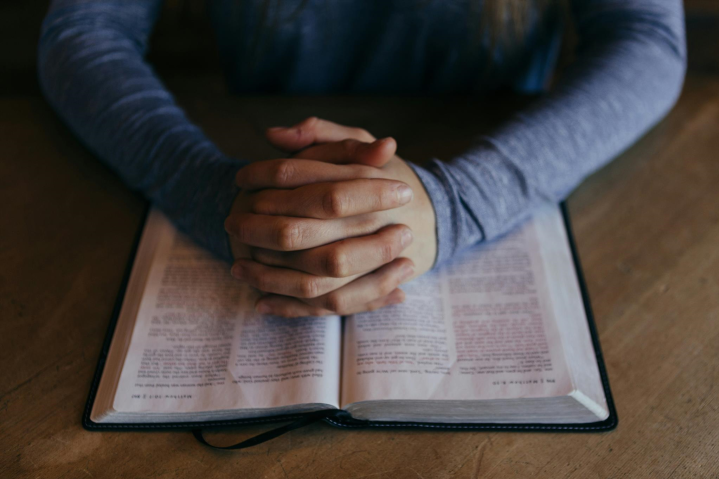 A person praying with hands resting on the Bible.